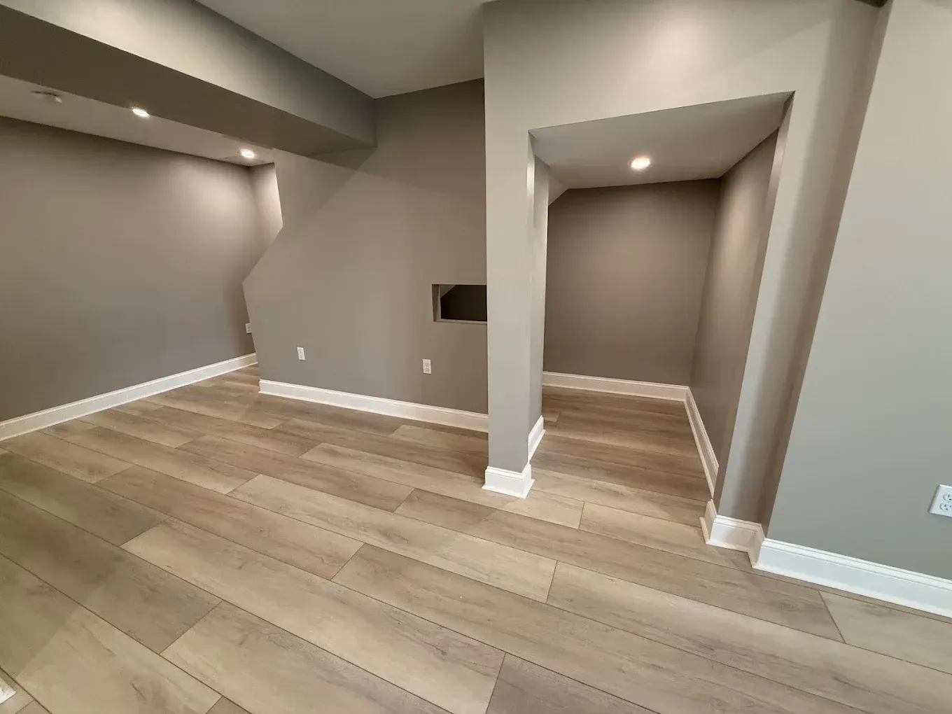 Gray-painted basement room with light wood-look flooring, recessed lighting, and a storage nook.