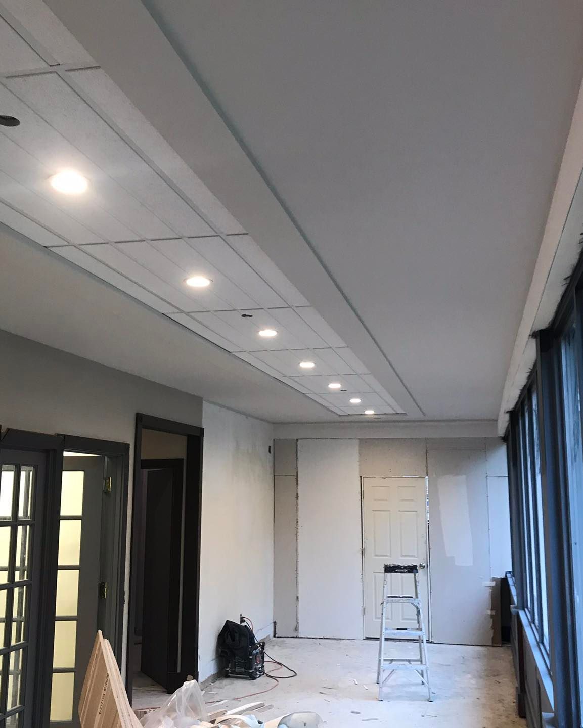 A hallway under construction with recessed ceiling lights, unfinished walls, and a ladder.