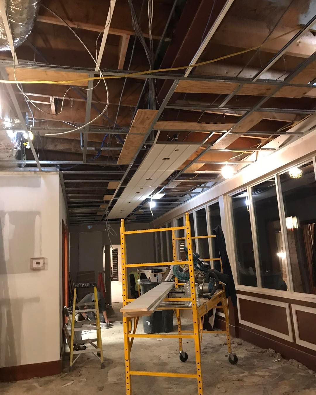 Interior construction site with exposed ceiling structure, scaffolding, and unfinished walls.