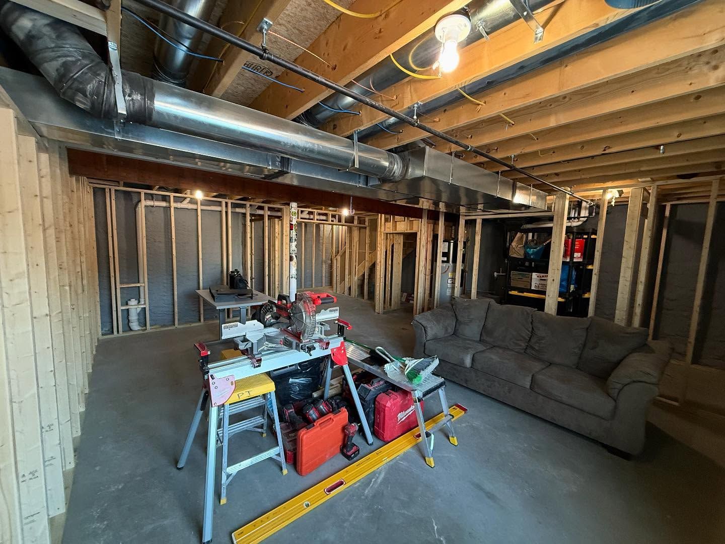 Basement under construction with framing, tools, a sofa, and exposed ductwork overhead.