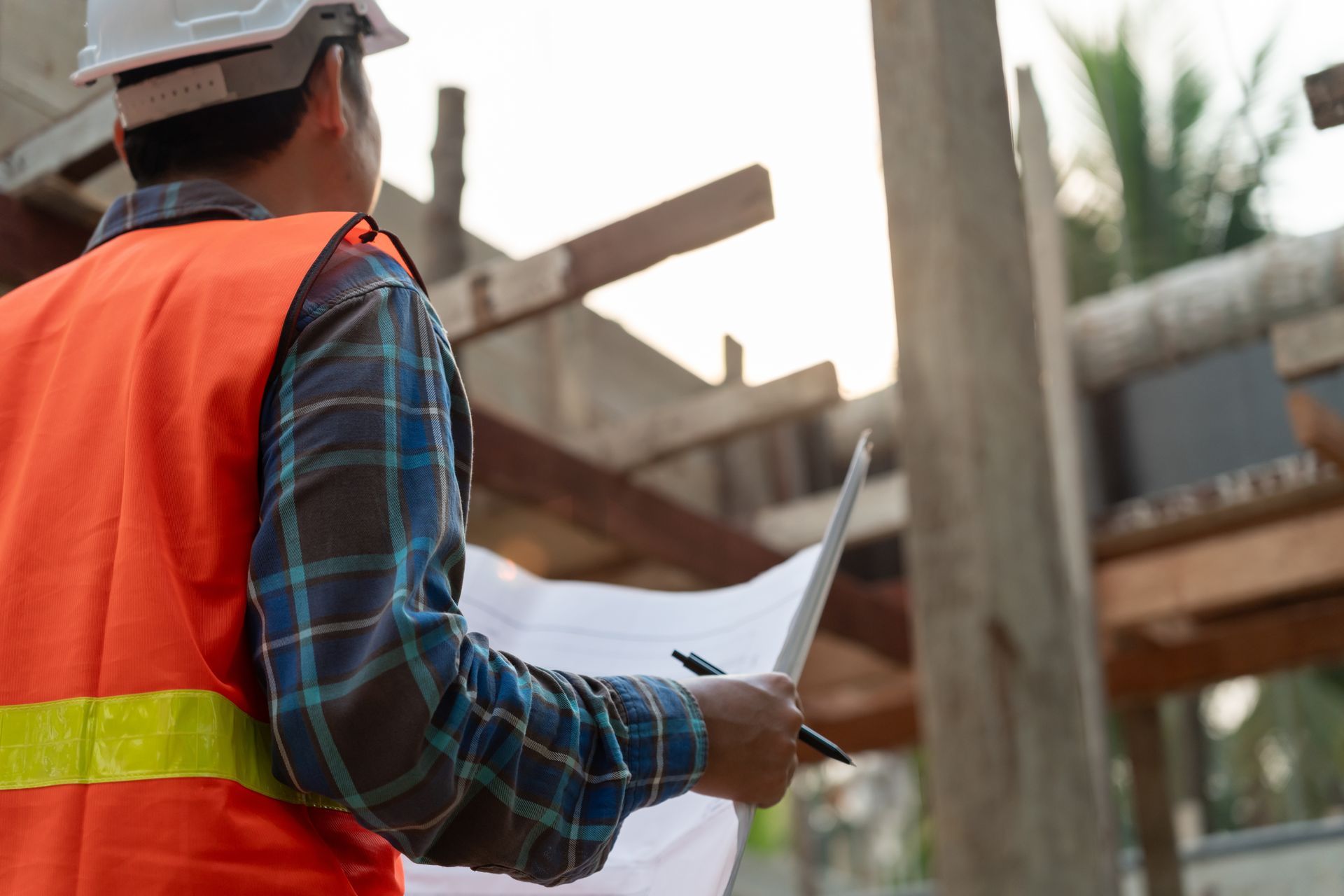A person in a hard hat and high-visibility vest reviews blueprints on a construction site.