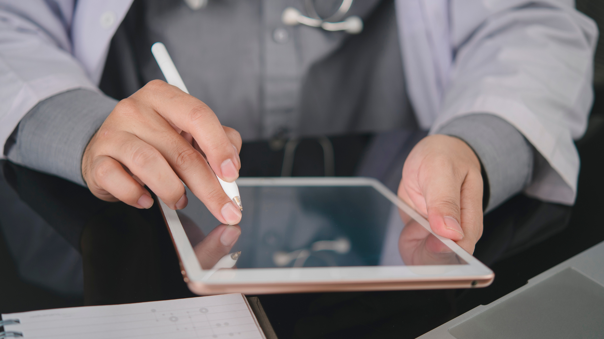 Doctor using a stylus on a tablet, writing in white coat.