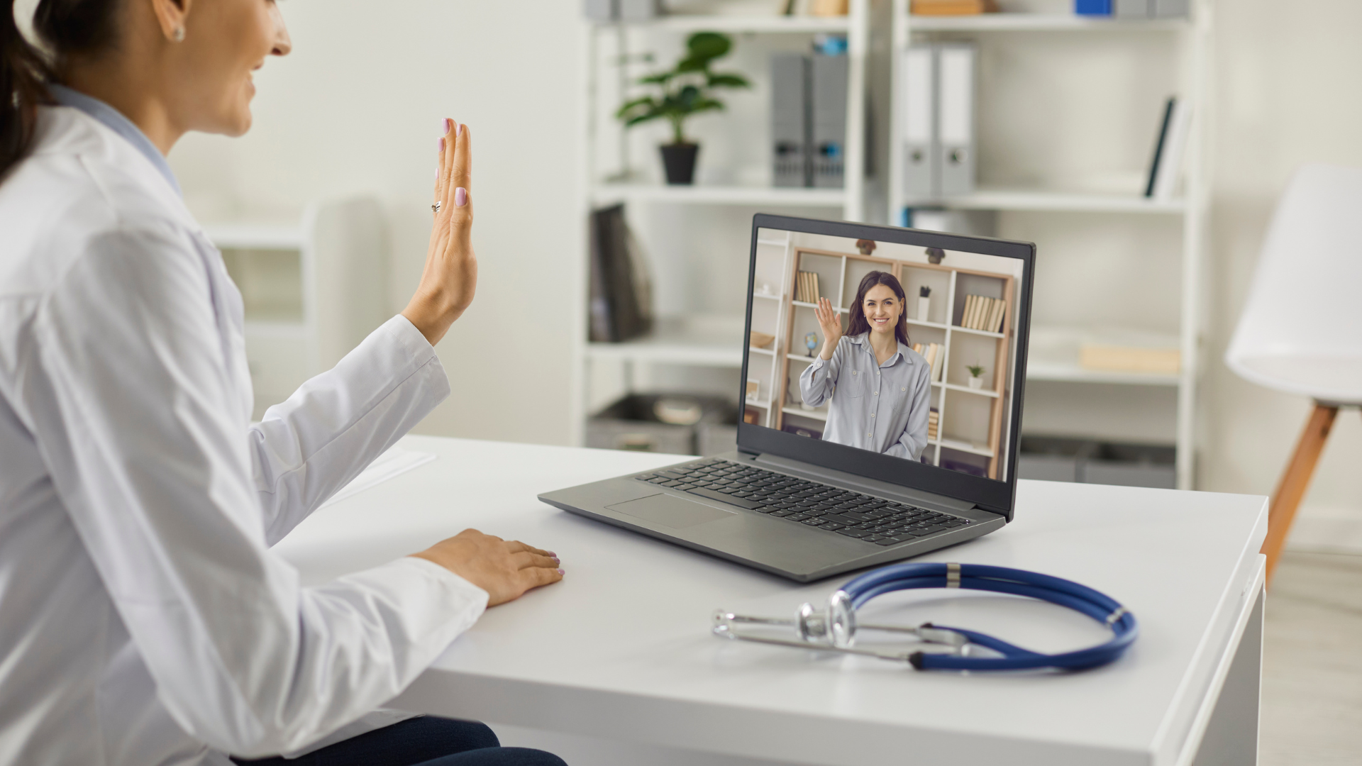 Doctor waving to patient on a laptop during a telehealth appointment.