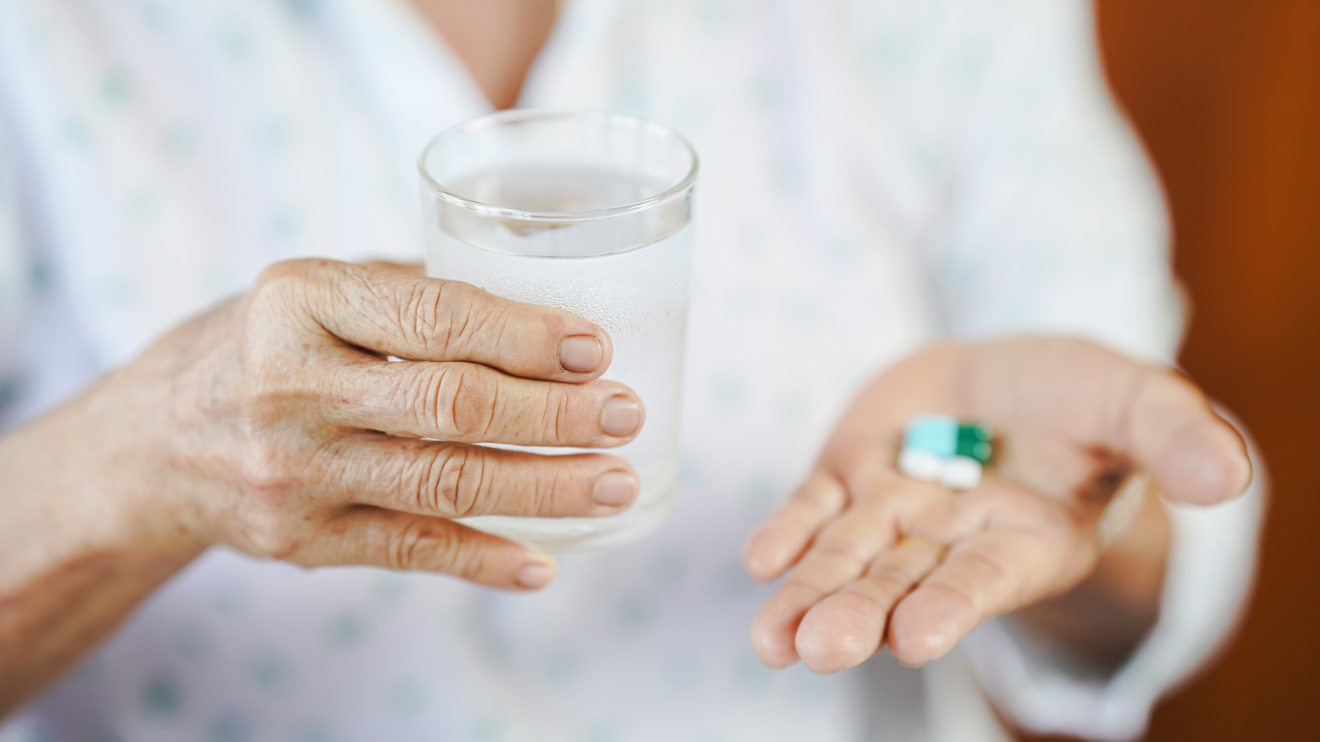 Person holding a glass of water and pills in their palm.