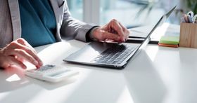 Man typing on a computer while using calculator representing payroll processing, financial analysis