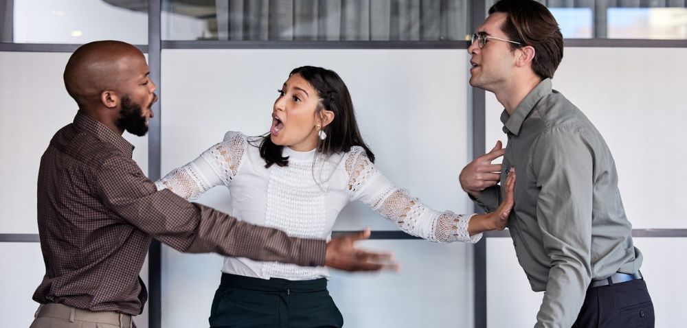 Two men argue while a woman stands between them, trying to mediate a workplace conflict