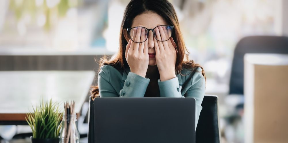 Professional woman at laptop rubbing eyes, representing workplace stress and HR decision challenges.