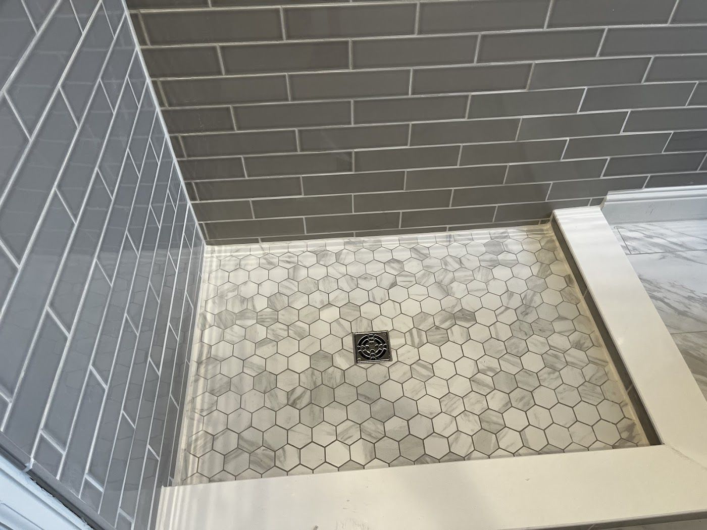 A shower stall with a hexagonal tile floor and a drain.