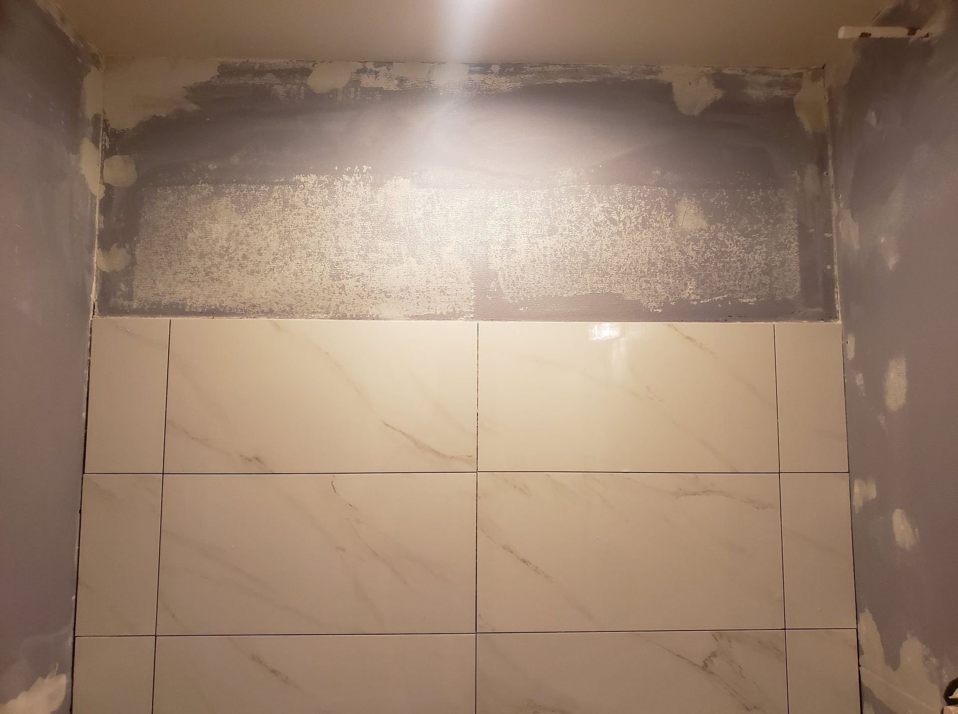 A bathroom with white tiles being installed on the wall.