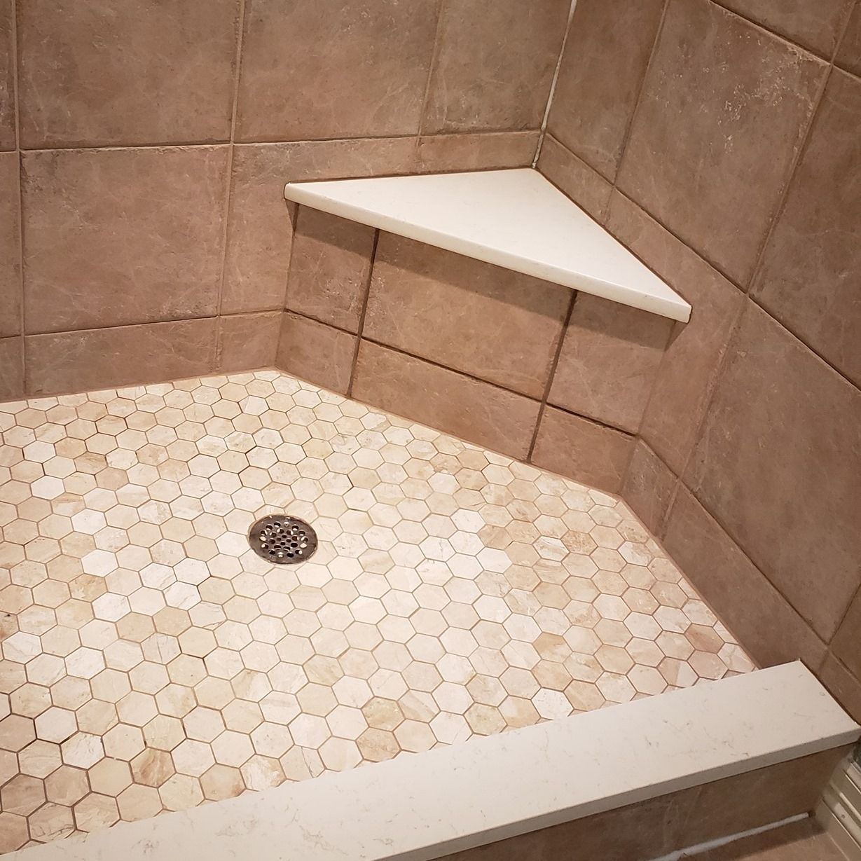 A shower stall with a corner shelf and a drain