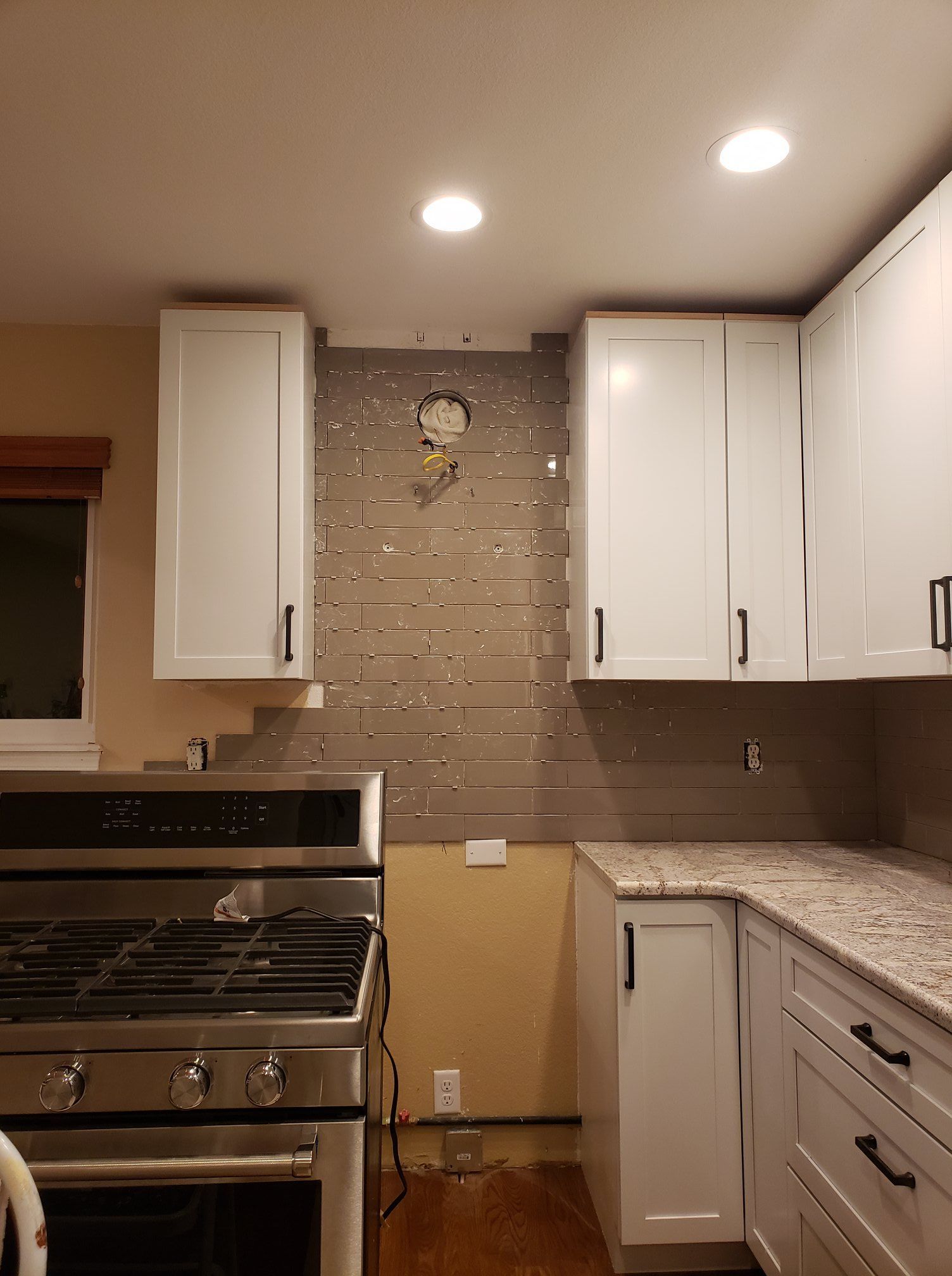 A kitchen with white cabinets , a stove , and a clock on the wall.