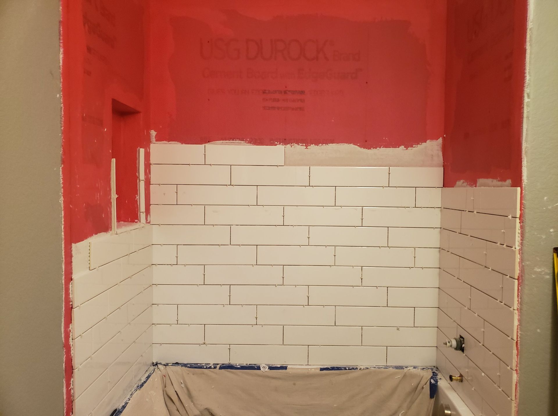 A bathroom with white tiles and a red wall that says usg durock