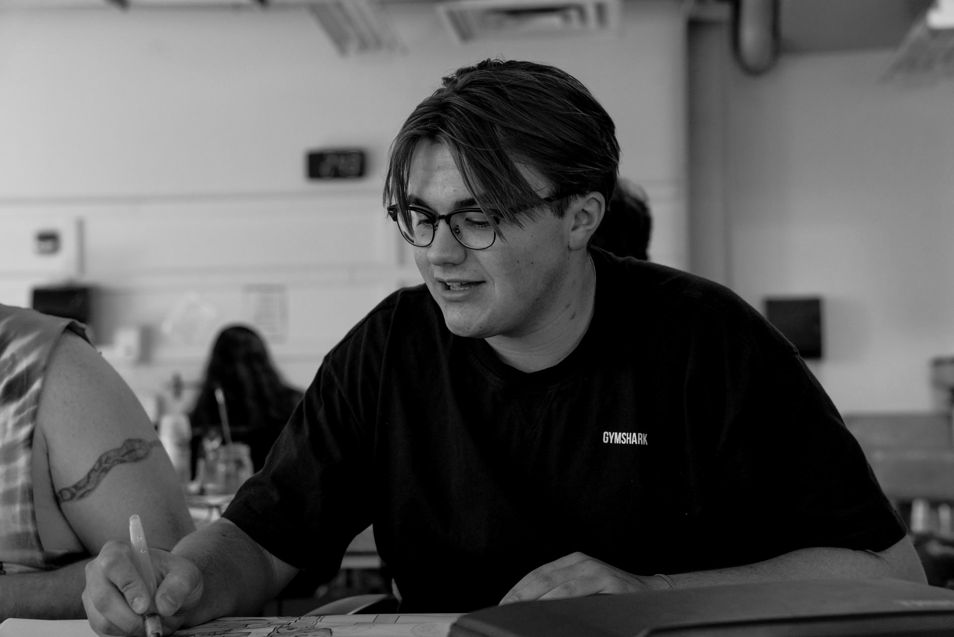 A man wearing glasses is sitting at a table writing on a piece of paper.