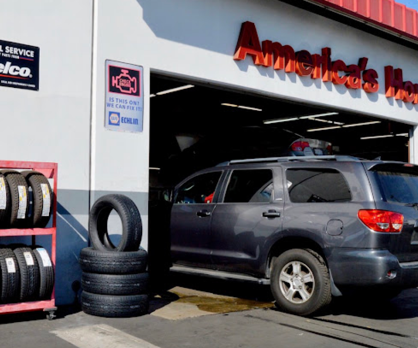 SUV in an auto repair shop bay beside stacked tires and a service sign | Lee Rollins Firestone