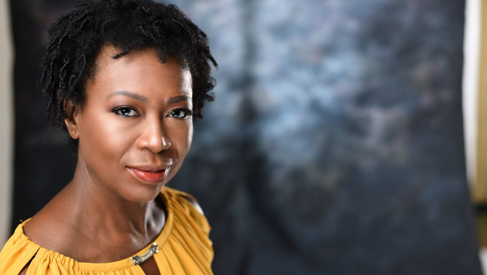 A woman in a yellow shirt is smiling and looking at the camera.