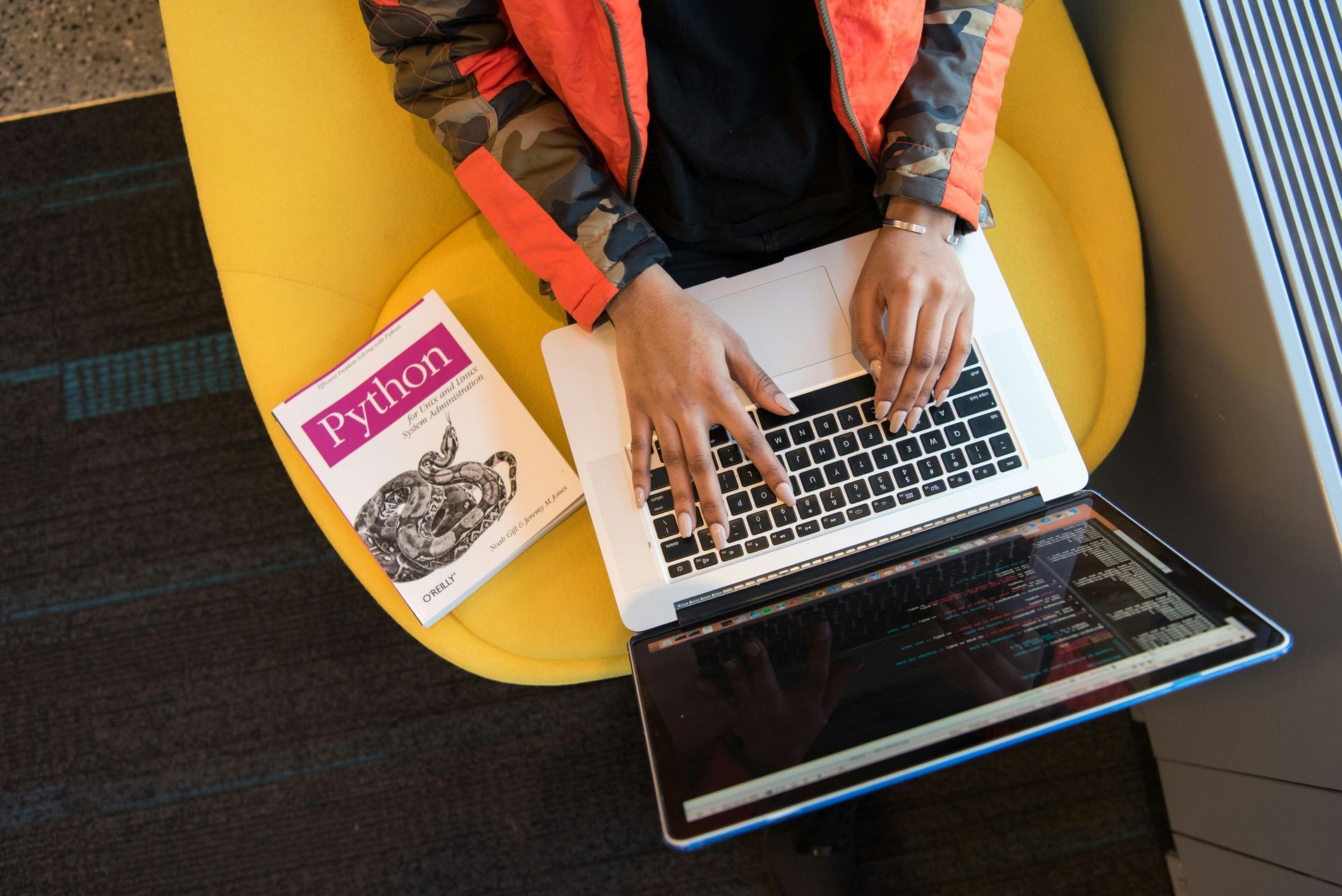 A person is typing on a laptop next to a book about python.