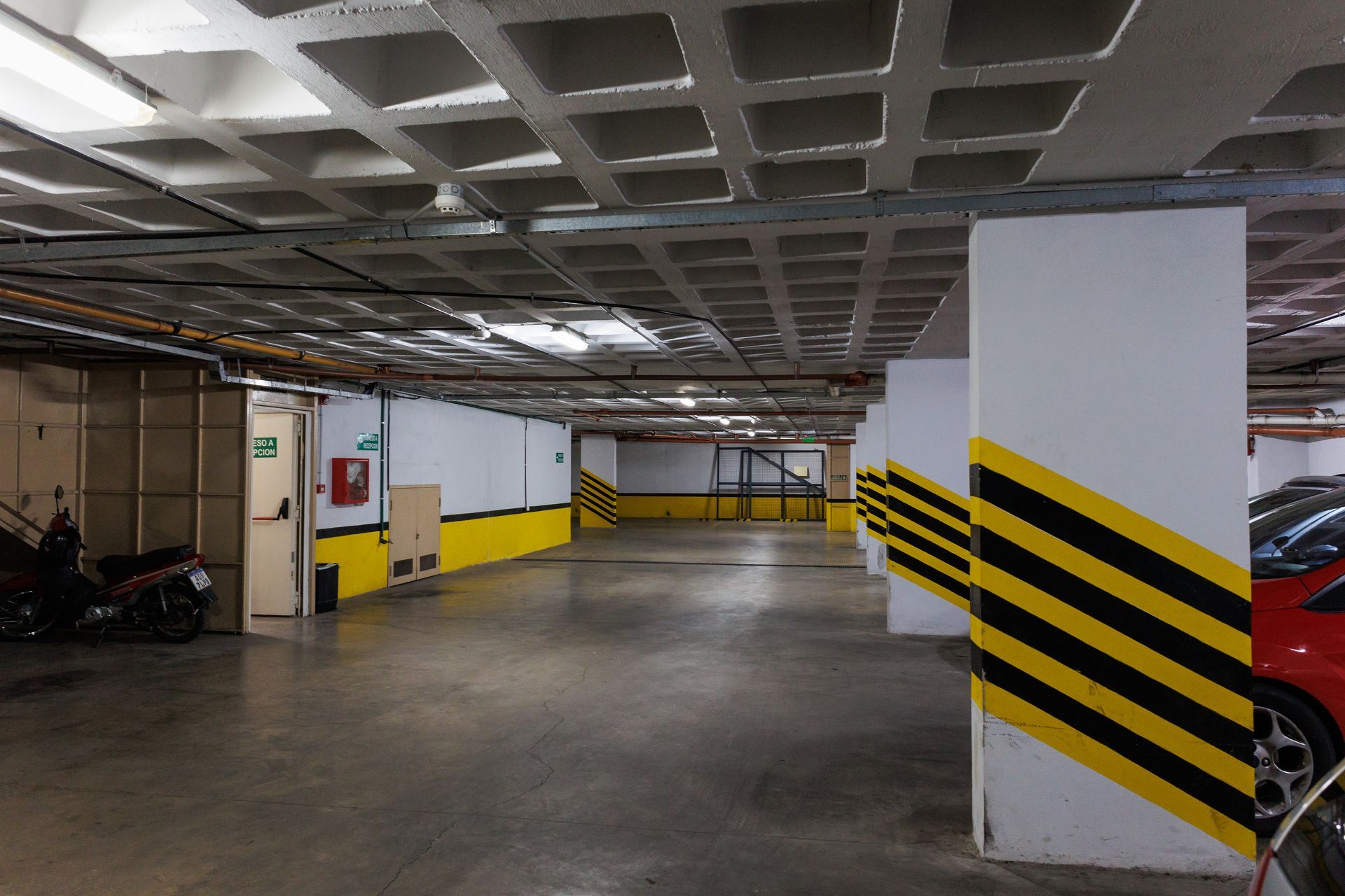 Interior de un estacionamiento subterráneo con pilares de rayas amarillas y negras y paredes blancas.