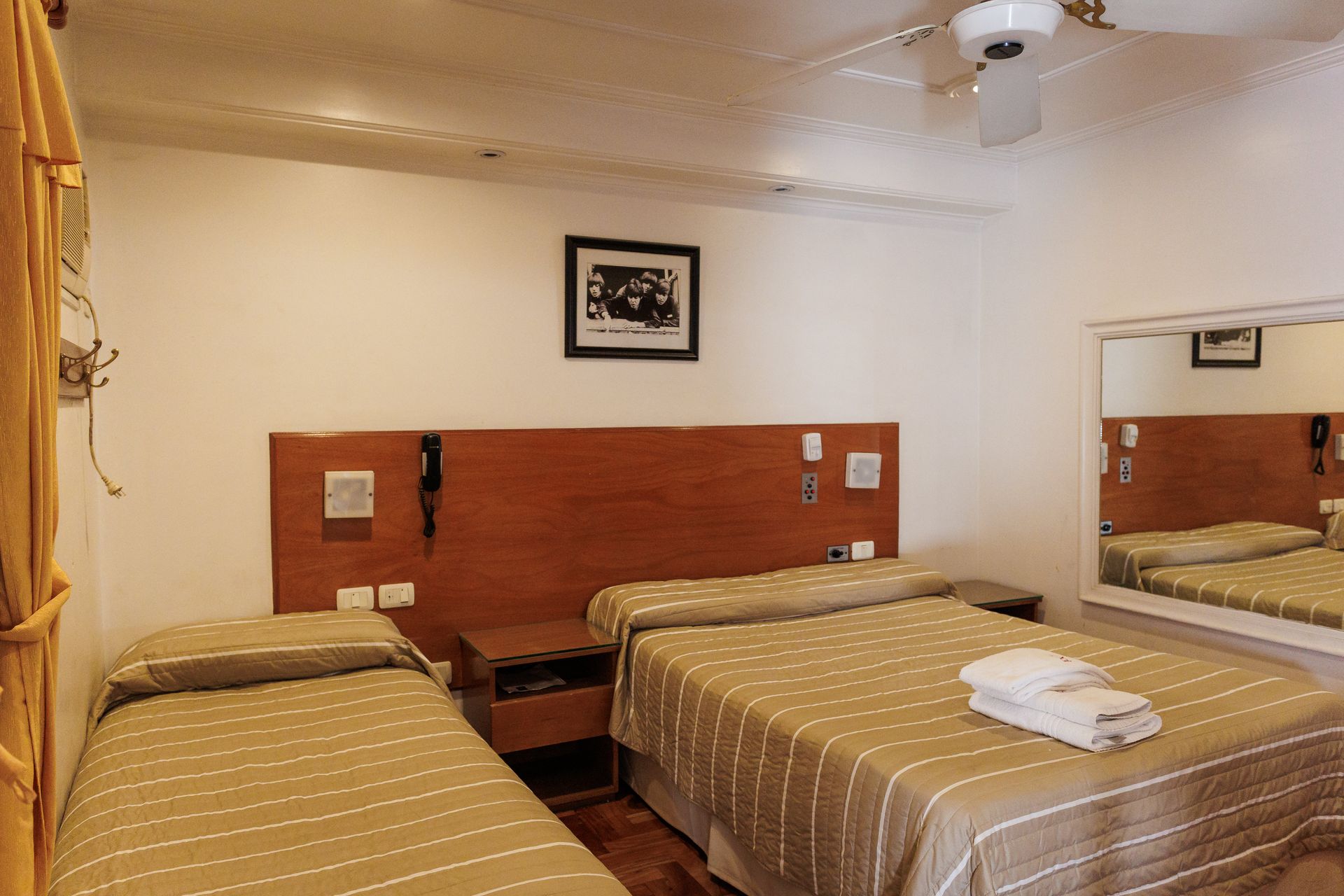 Habitación de hotel con cama doble, dos camas individuales y espejo. Combinación de colores beige y marrón.