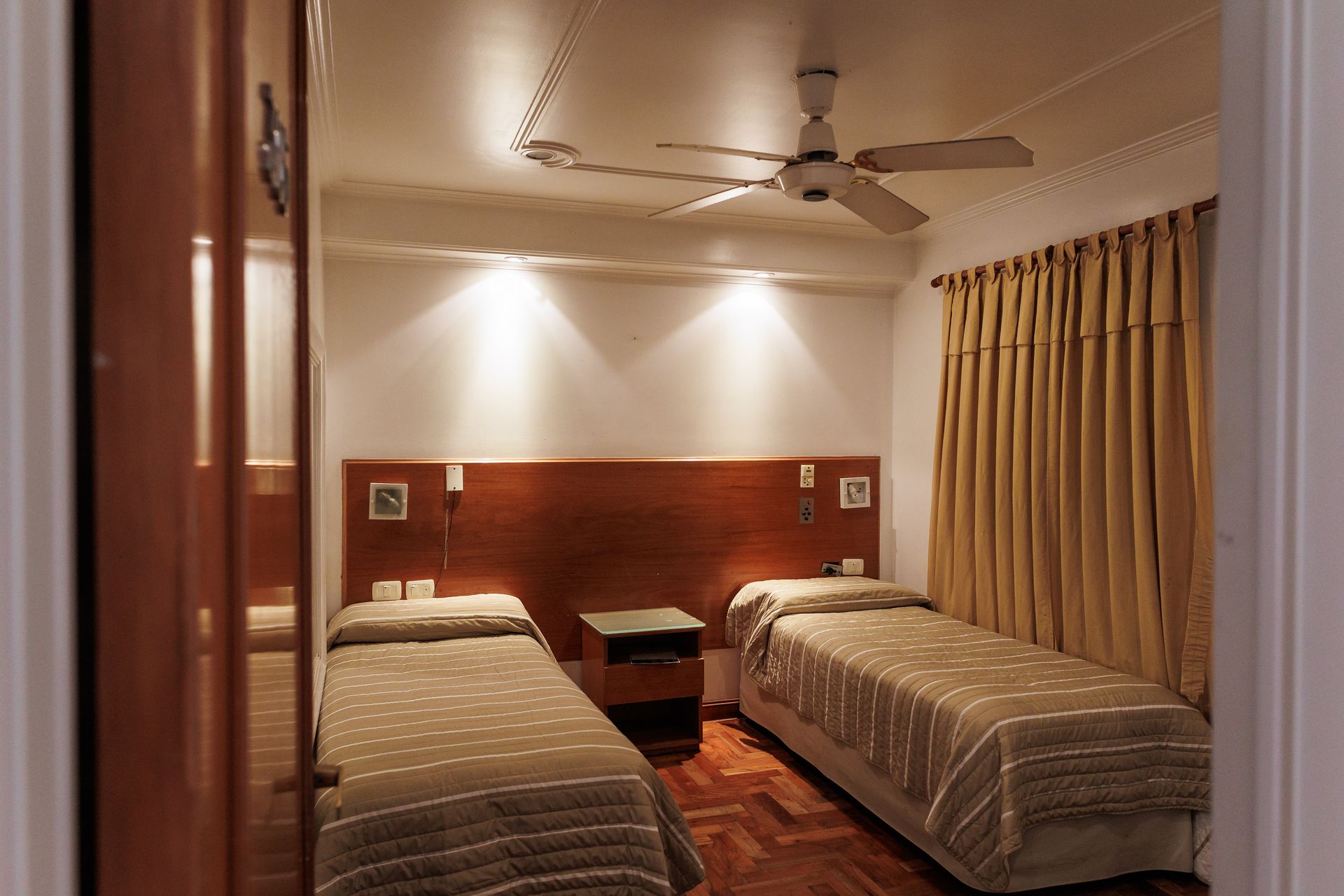Camas individuales en una habitación de hotel. Tonos marrones y dorados, muebles de madera.