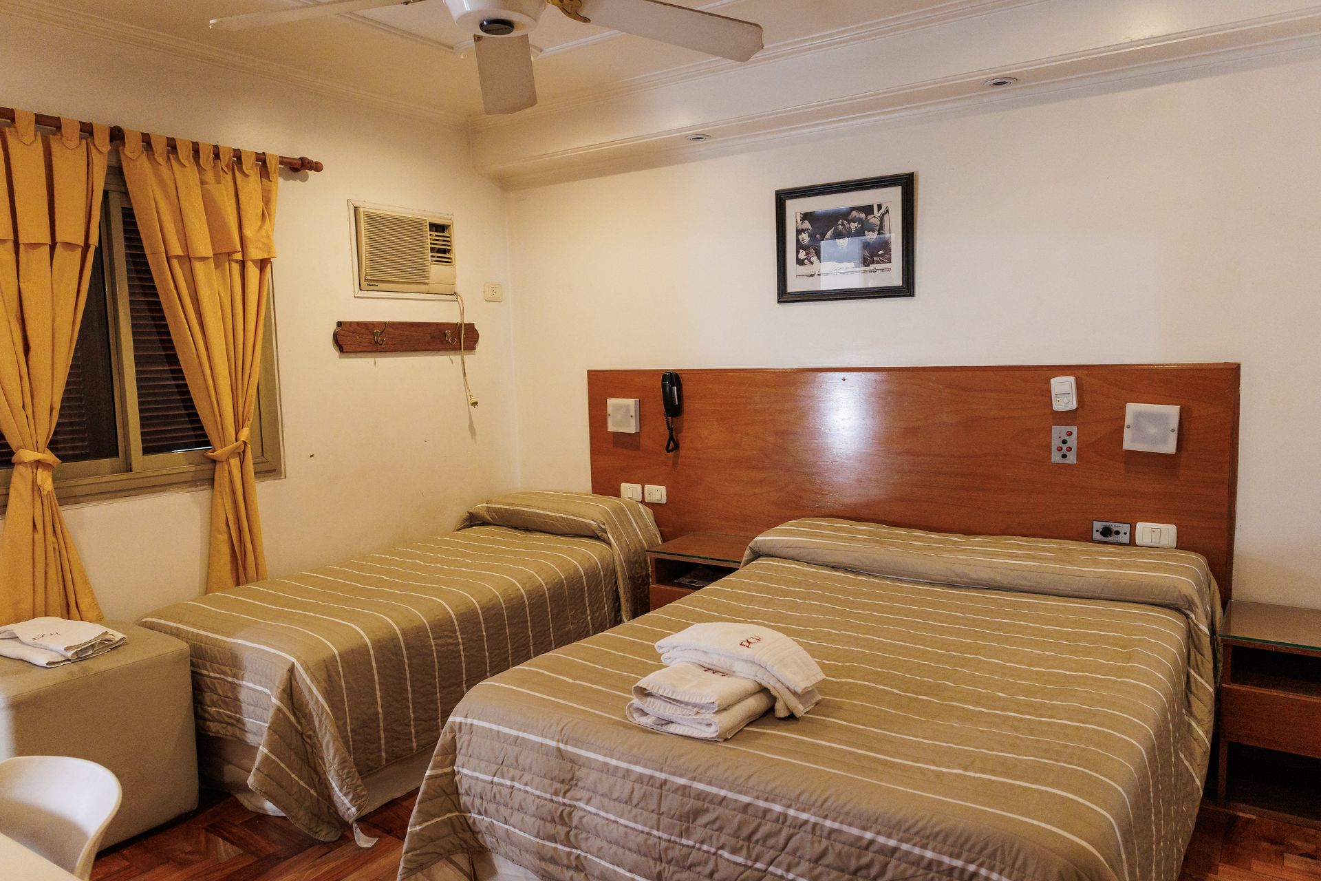 Habitación de hotel con dos camas, cortinas amarillas y aire acondicionado.