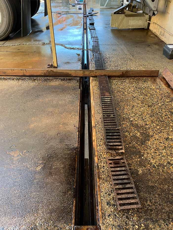 A close up of a drain in a garage with a truck in the background.