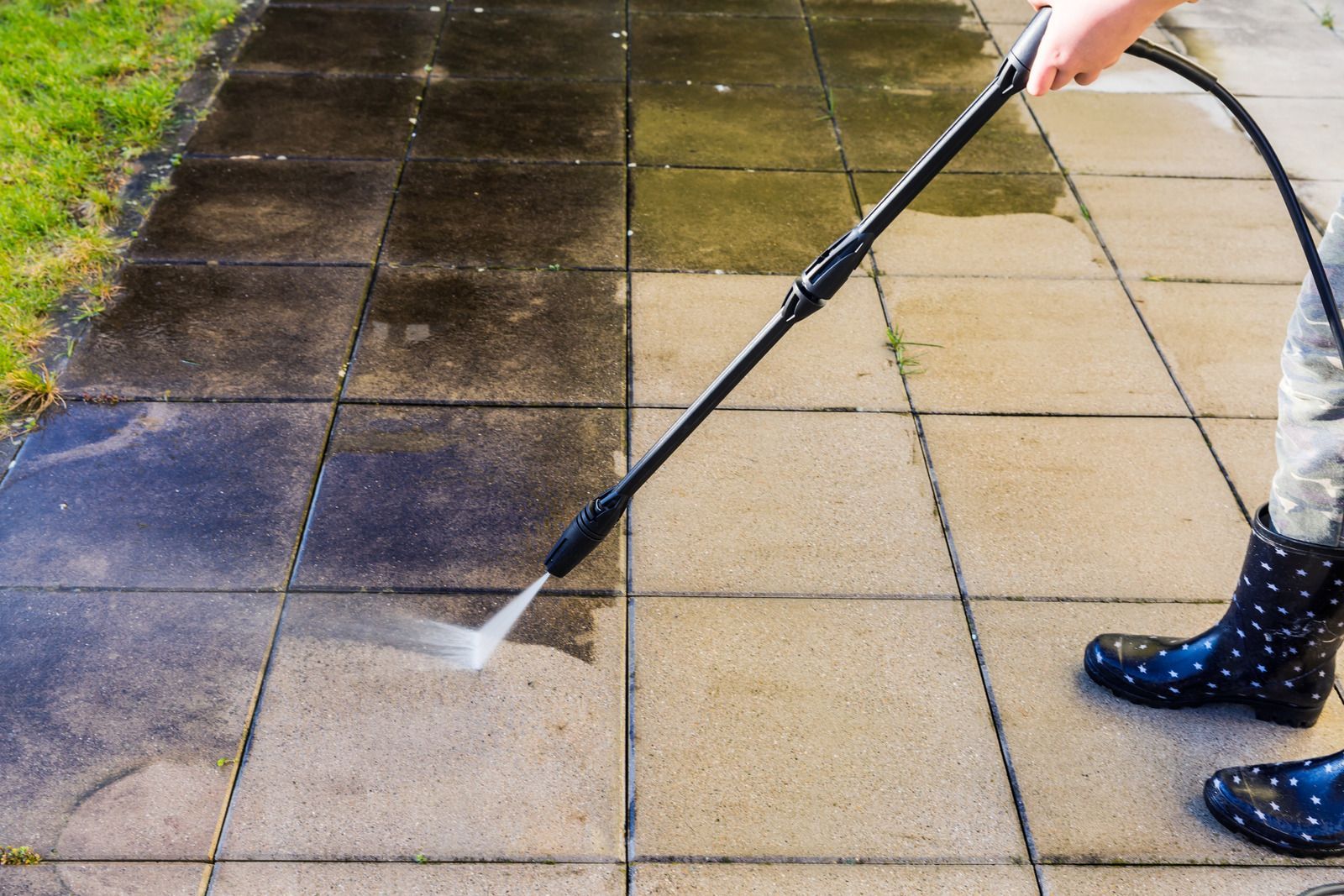 A person is cleaning a sidewalk with a high pressure washer.