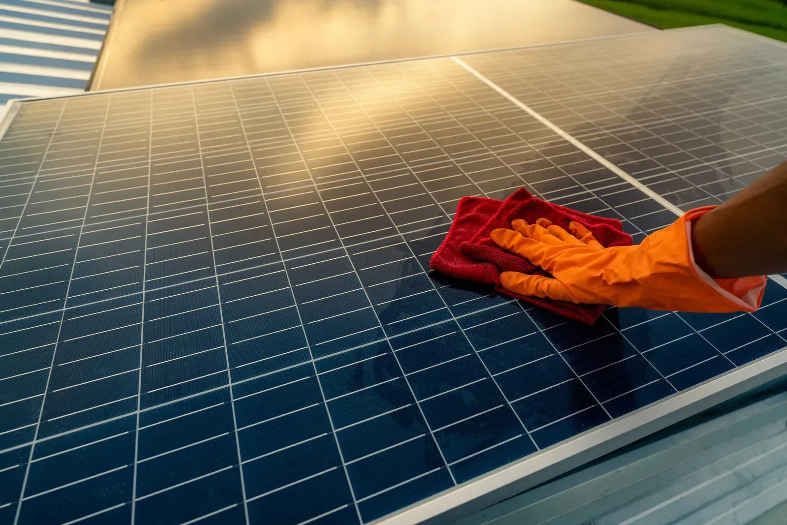 Person in orange gloves cleaning solar panel with a red cloth outdoors.