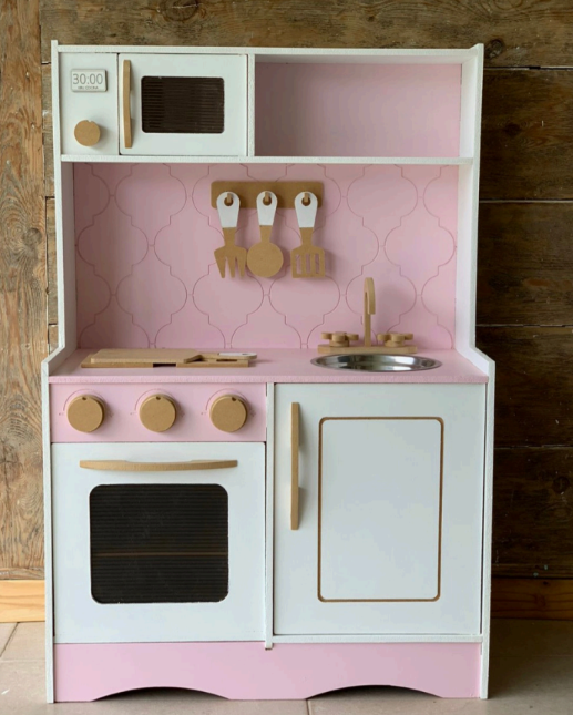 Cocina de juguete de madera rosa y blanca con horno, microondas y fregadero.