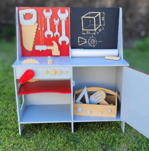 Banco de trabajo de juguete de madera para niños con herramientas, pizarra y armario abierto, sobre césped.