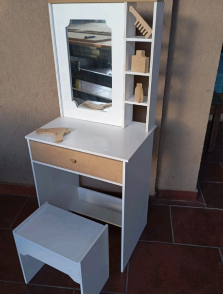 Tocador blanco y en tonos madera con espejo, estantes y taburete. Se exhiben un peine y pequeños objetos de madera.