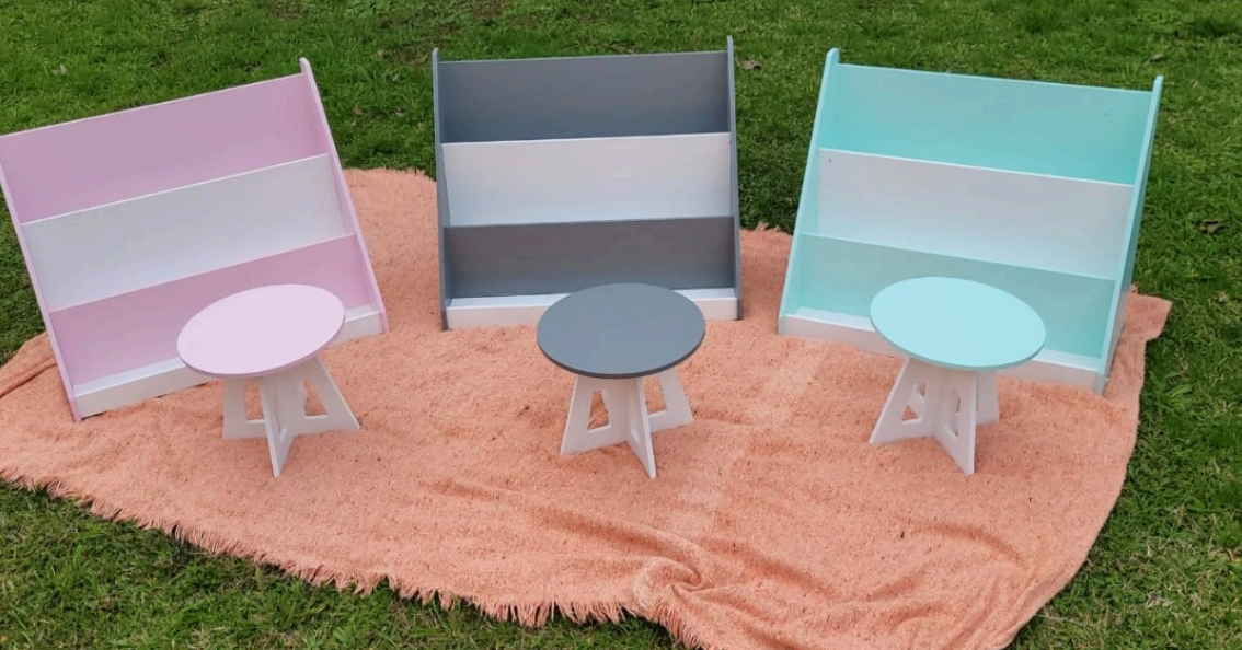 Tres pequeñas estanterías y taburetes pintados sobre una manta naranja sobre césped; rosa, gris y turquesa.