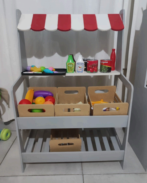 Puesto de mercado de juguete de madera con toldo rojo y blanco, estructura gris y artículos de comida de juguete.