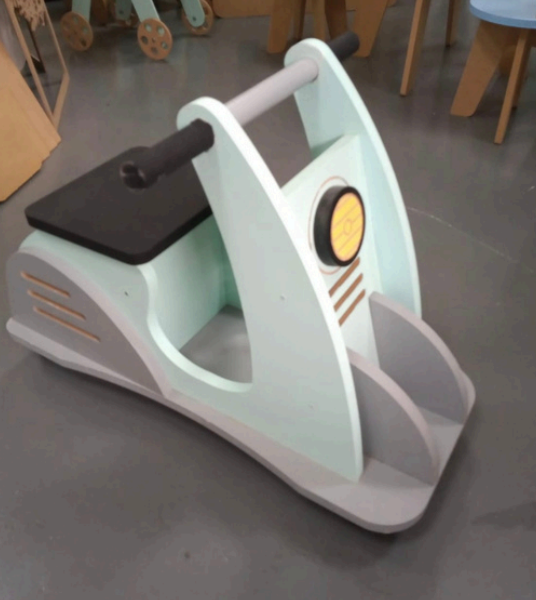 Patinete de juguete de madera, color verde menta con detalles en gris, asiento y manillar negros, faro amarillo.