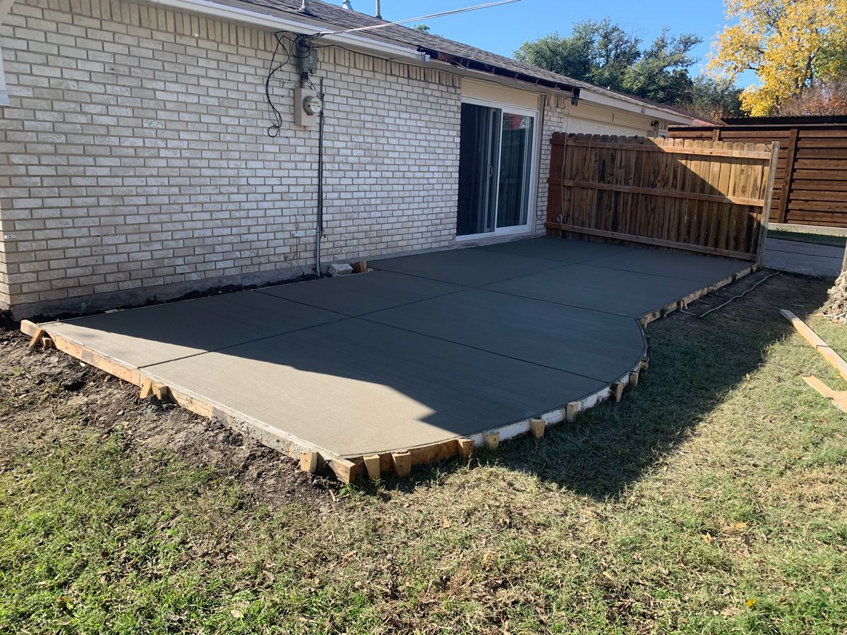 A concrete patio is being built in the backyard of a house.