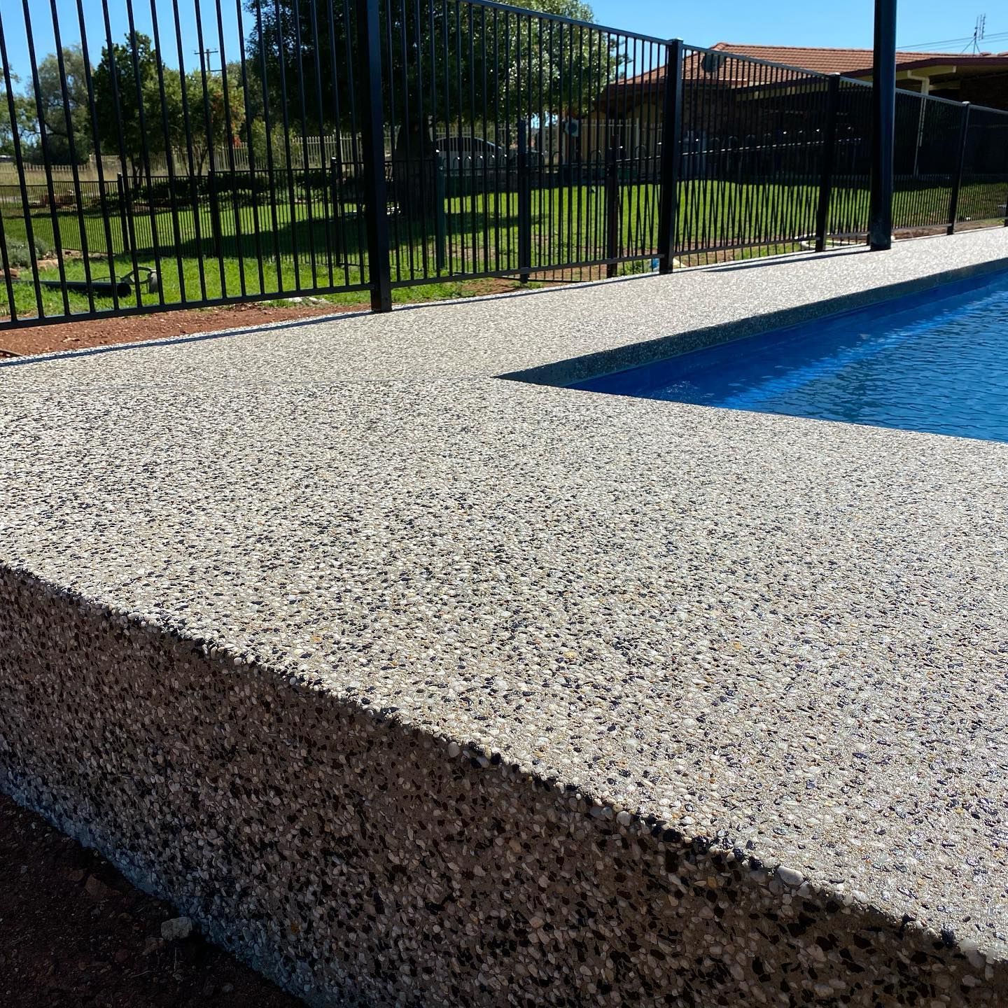 Poolside with textured concrete border, blue water, and black fence.