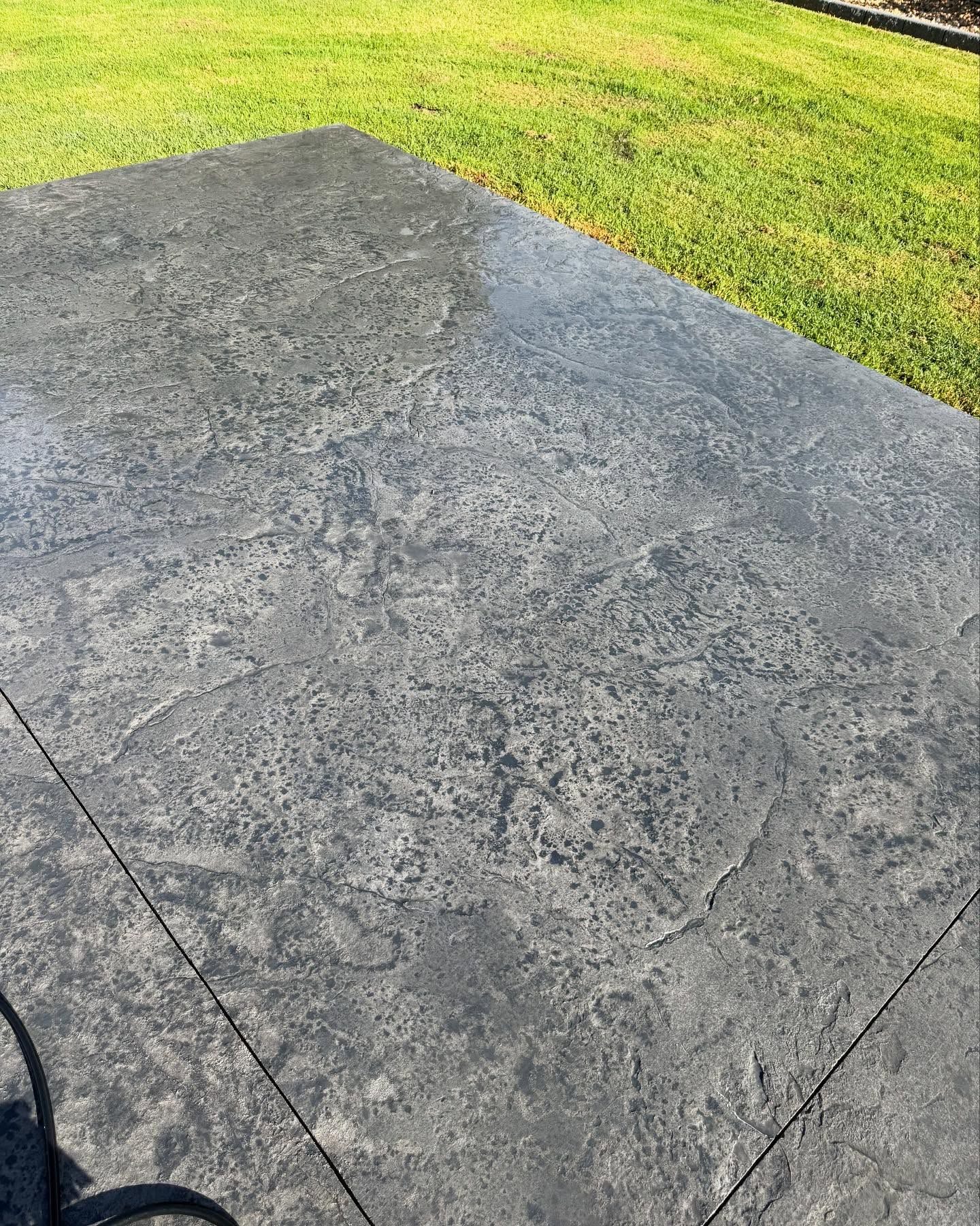 Dark gray stamped concrete patio with green grass in the background.