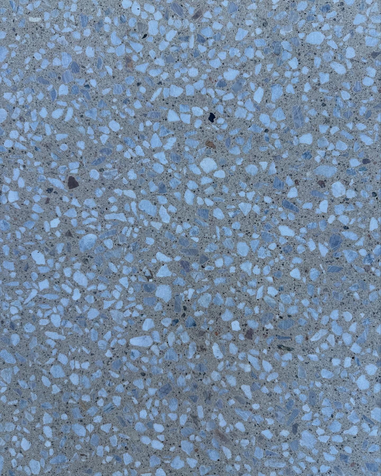 Close-up of a speckled, light gray surface with small, light blue and white aggregate stones.