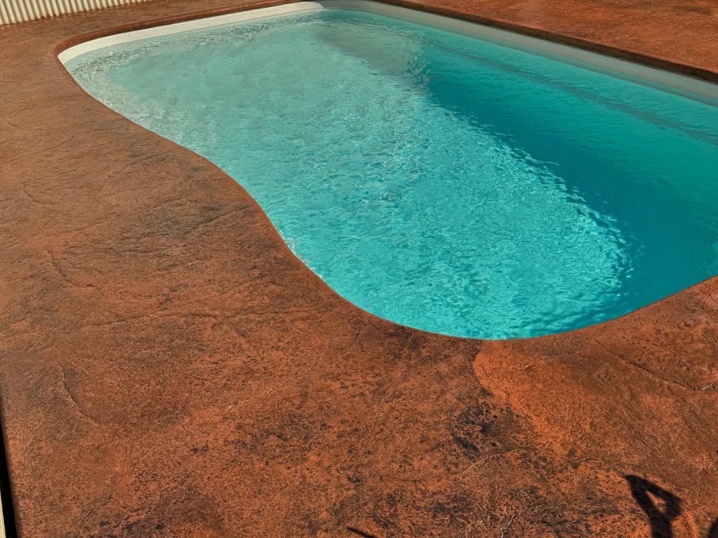 Pool with brown textured concrete surrounding it, turquoise water.