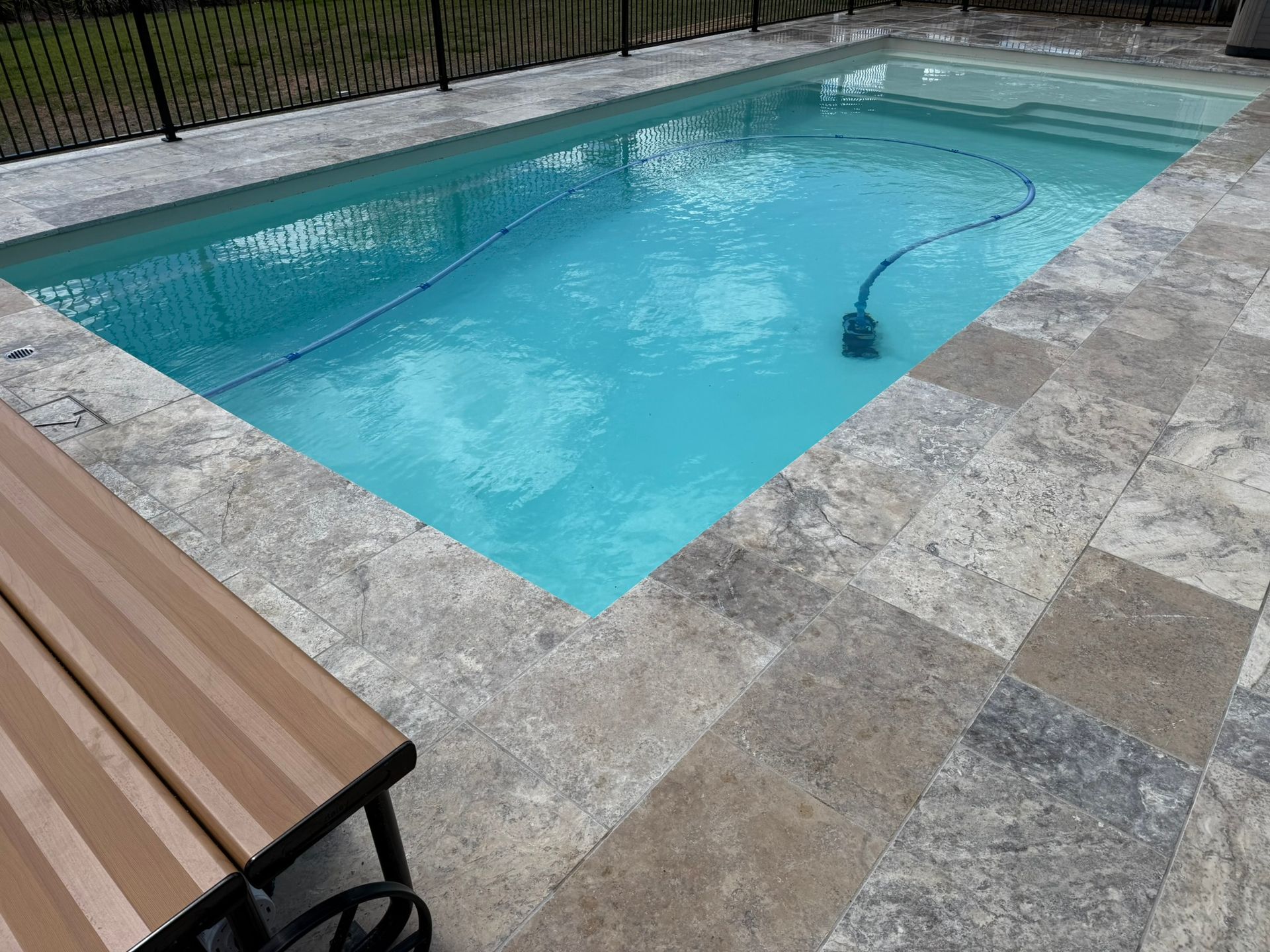 Rectangular swimming pool with blue water surrounded by stone pavers, bench in foreground.