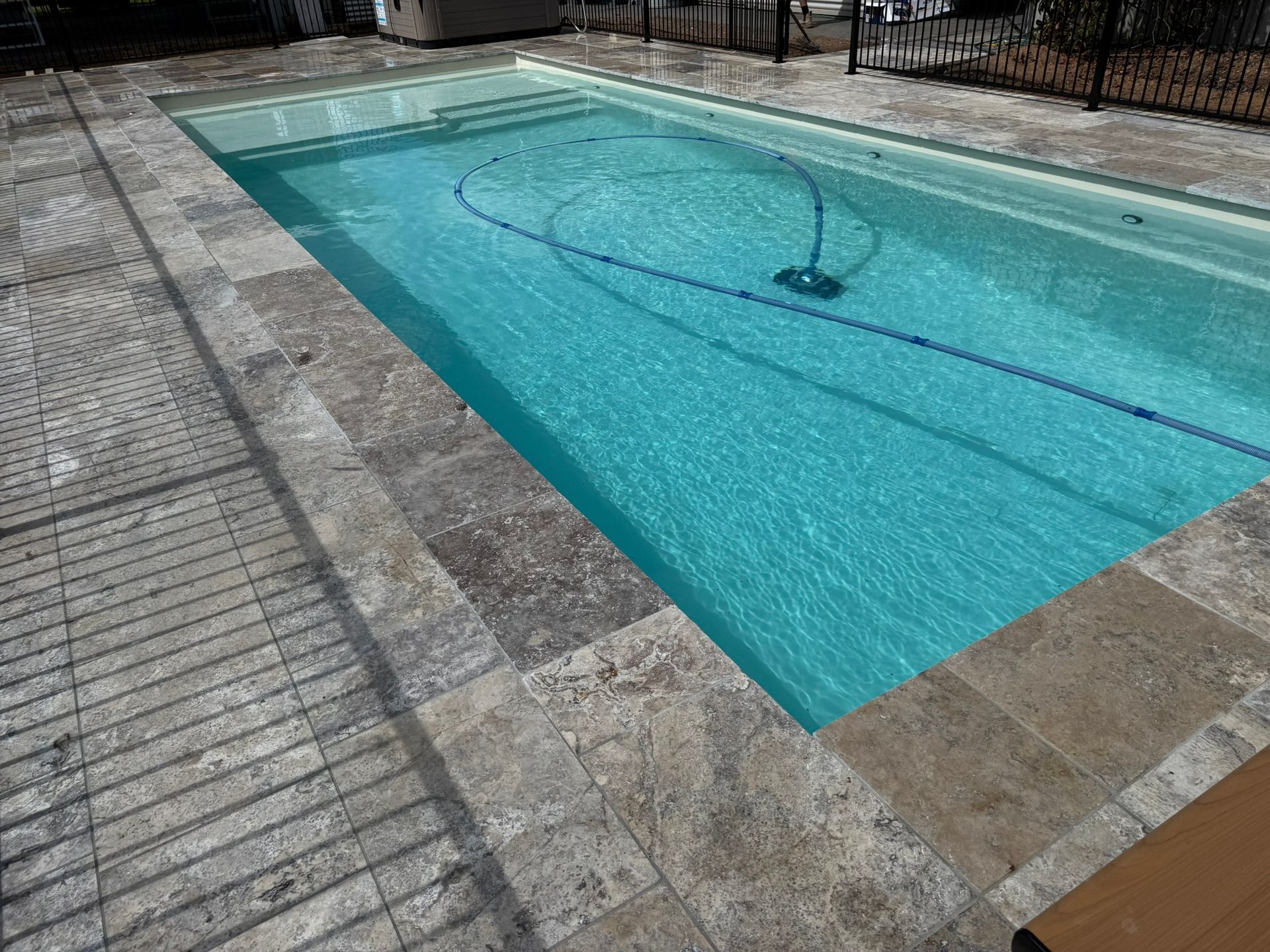 Rectangular swimming pool with turquoise water and stone surround. A pool cleaner is in the water.