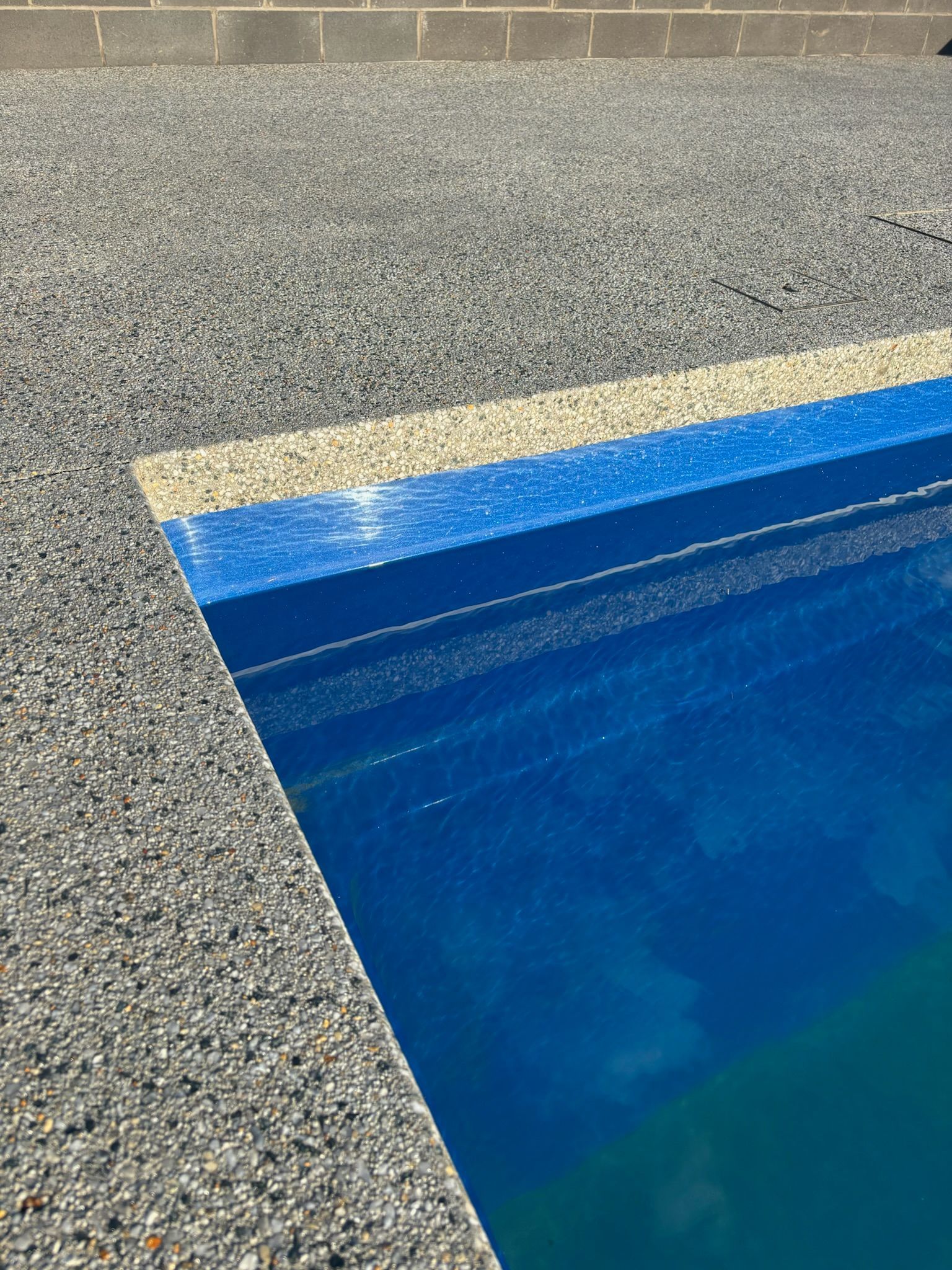 Pool edge with gray speckled concrete, blue water, and bordering stripe.