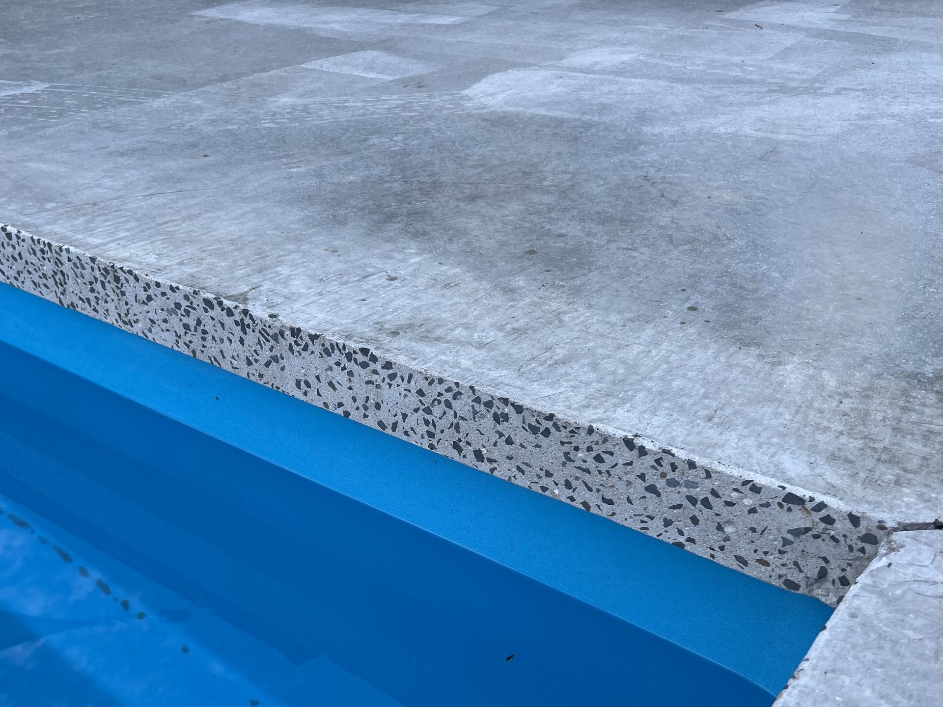 Concrete edge of a pool with a blue interior and a textured border.