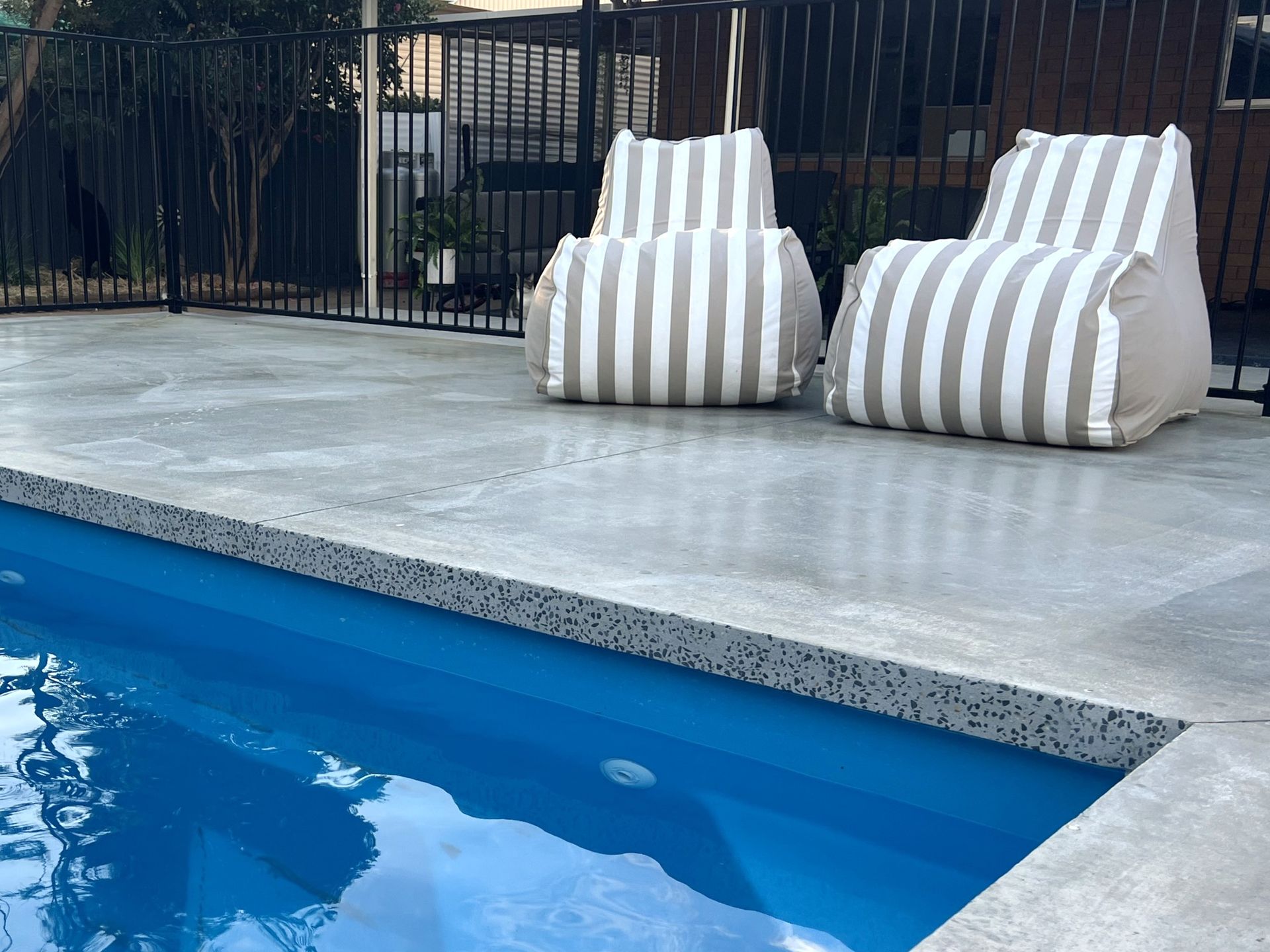 Poolside scene: two striped beanbag chairs on a gray concrete patio near a blue pool.