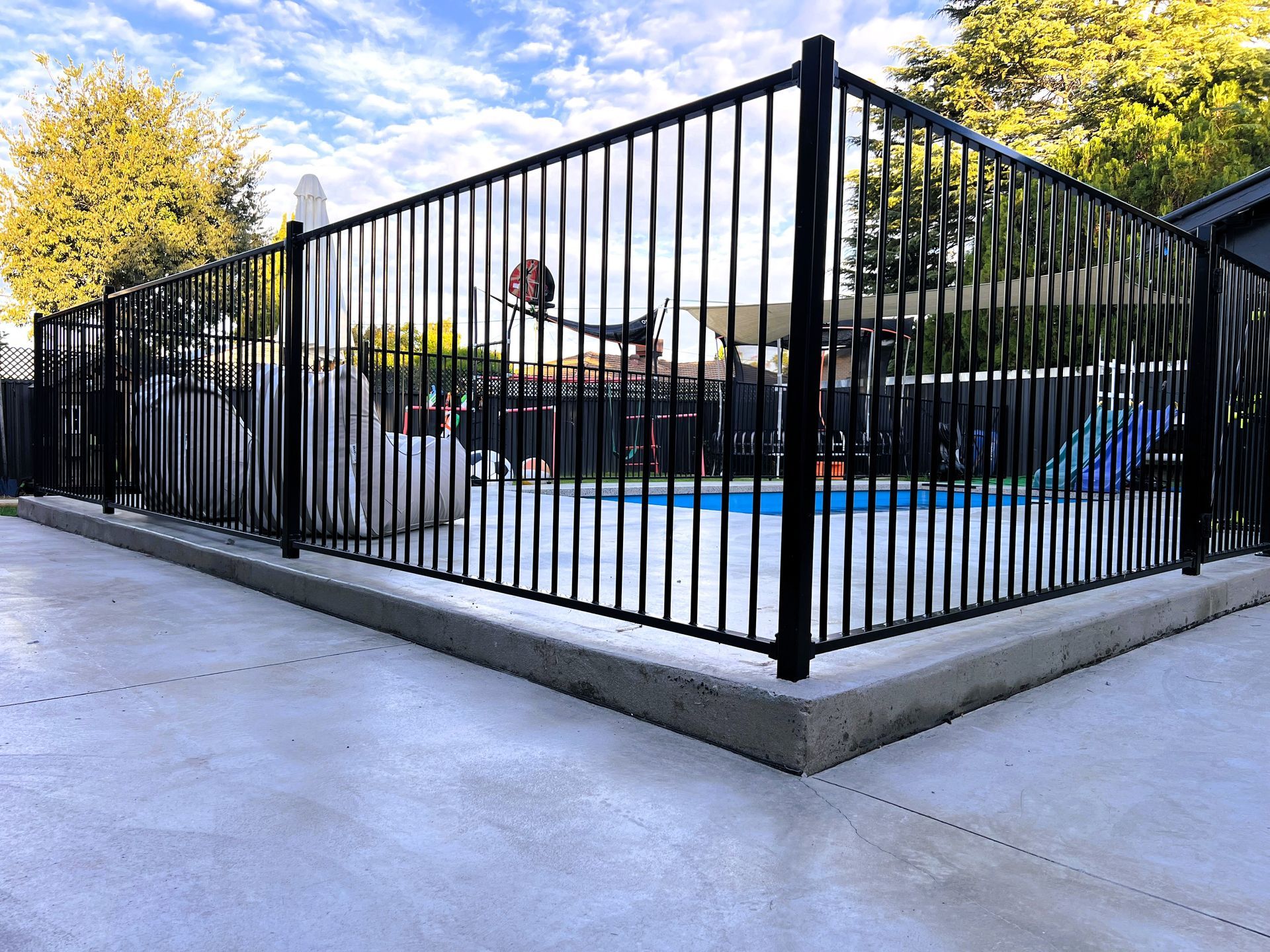 Black metal fence surrounding a pool in a backyard with a concrete patio.