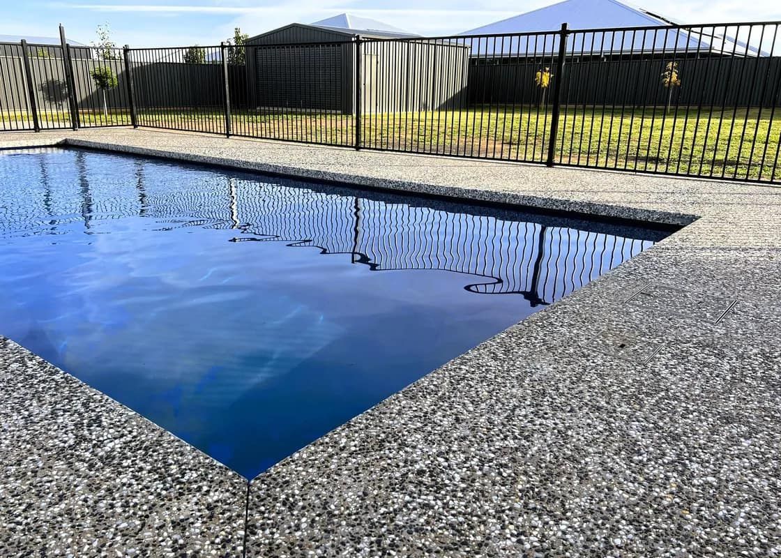 Swimming pool with black fence and concrete border, reflecting sky.