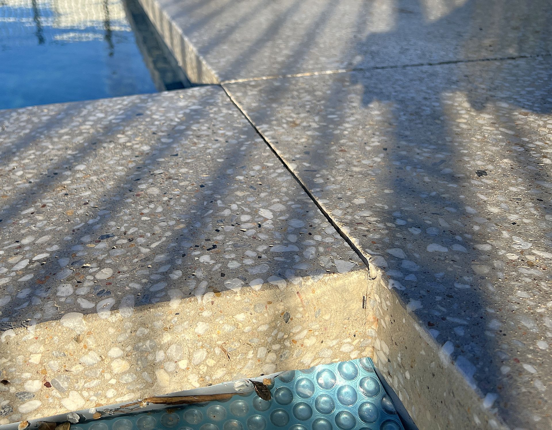 Concrete pool coping with a visible seam, partial view of water and a blue bubble wrap cover.