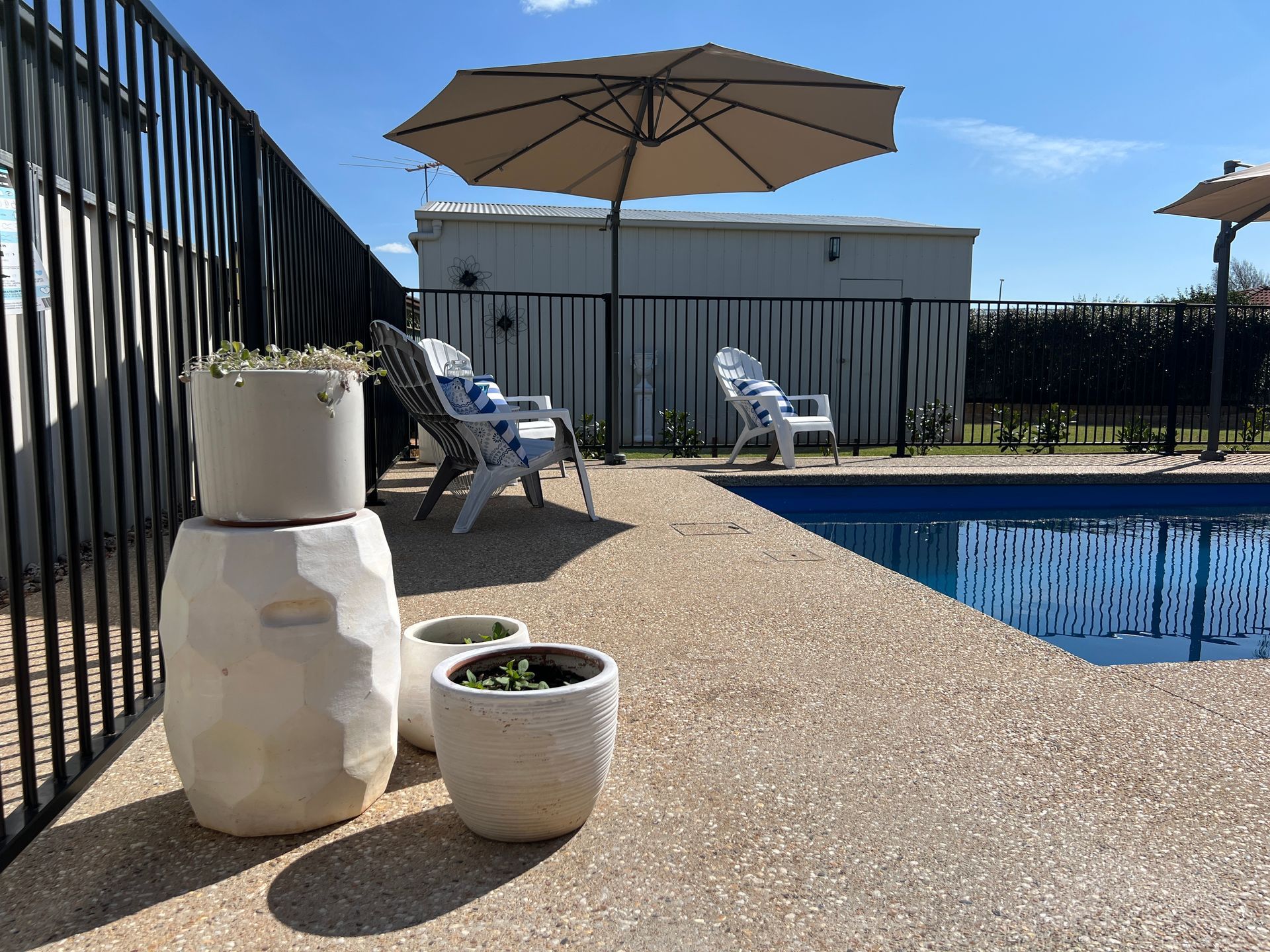Poolside scene: Beige umbrella shades two chairs; white pots on textured concrete.