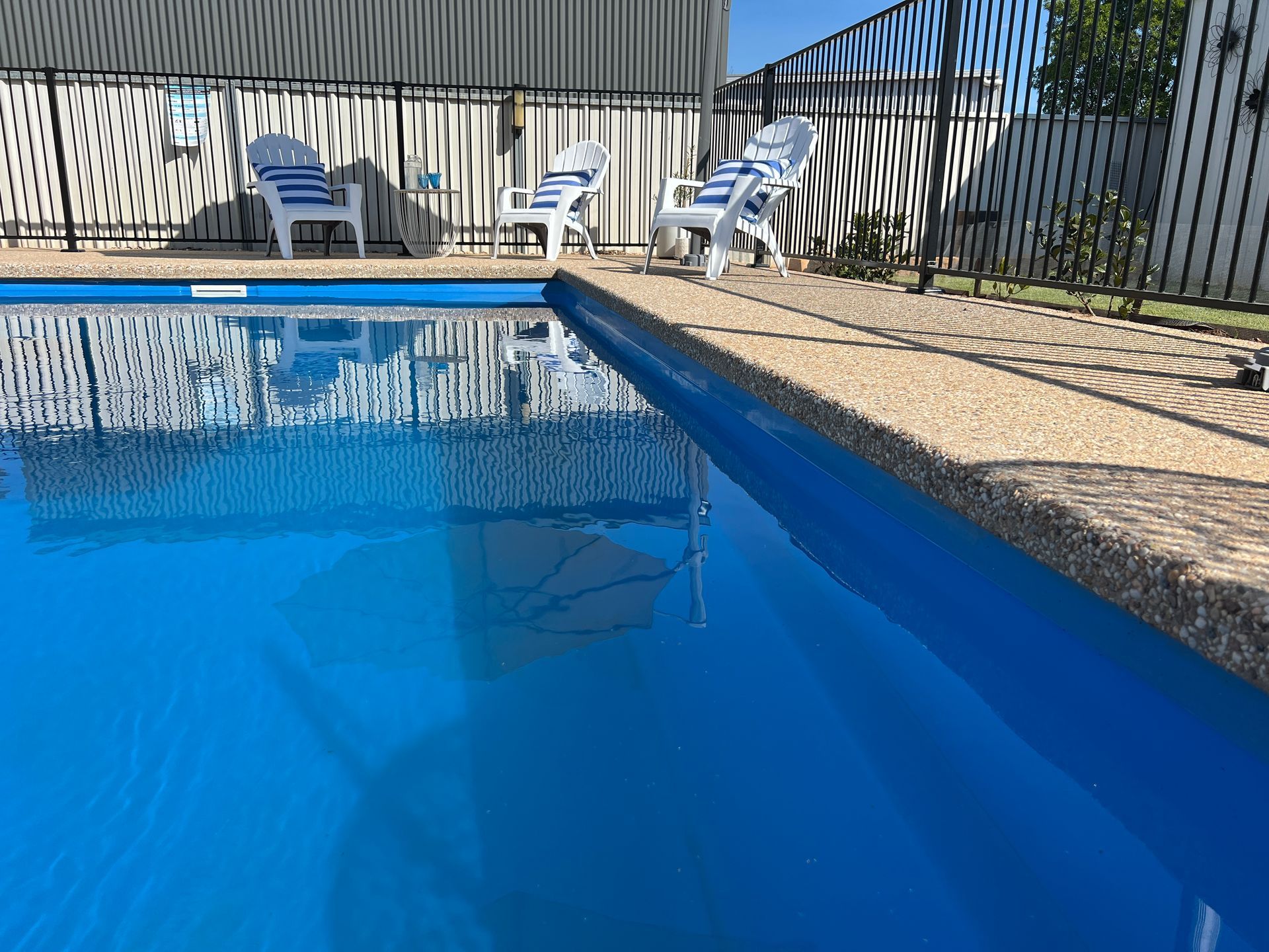 Blue swimming pool with lounge chairs and black fence.