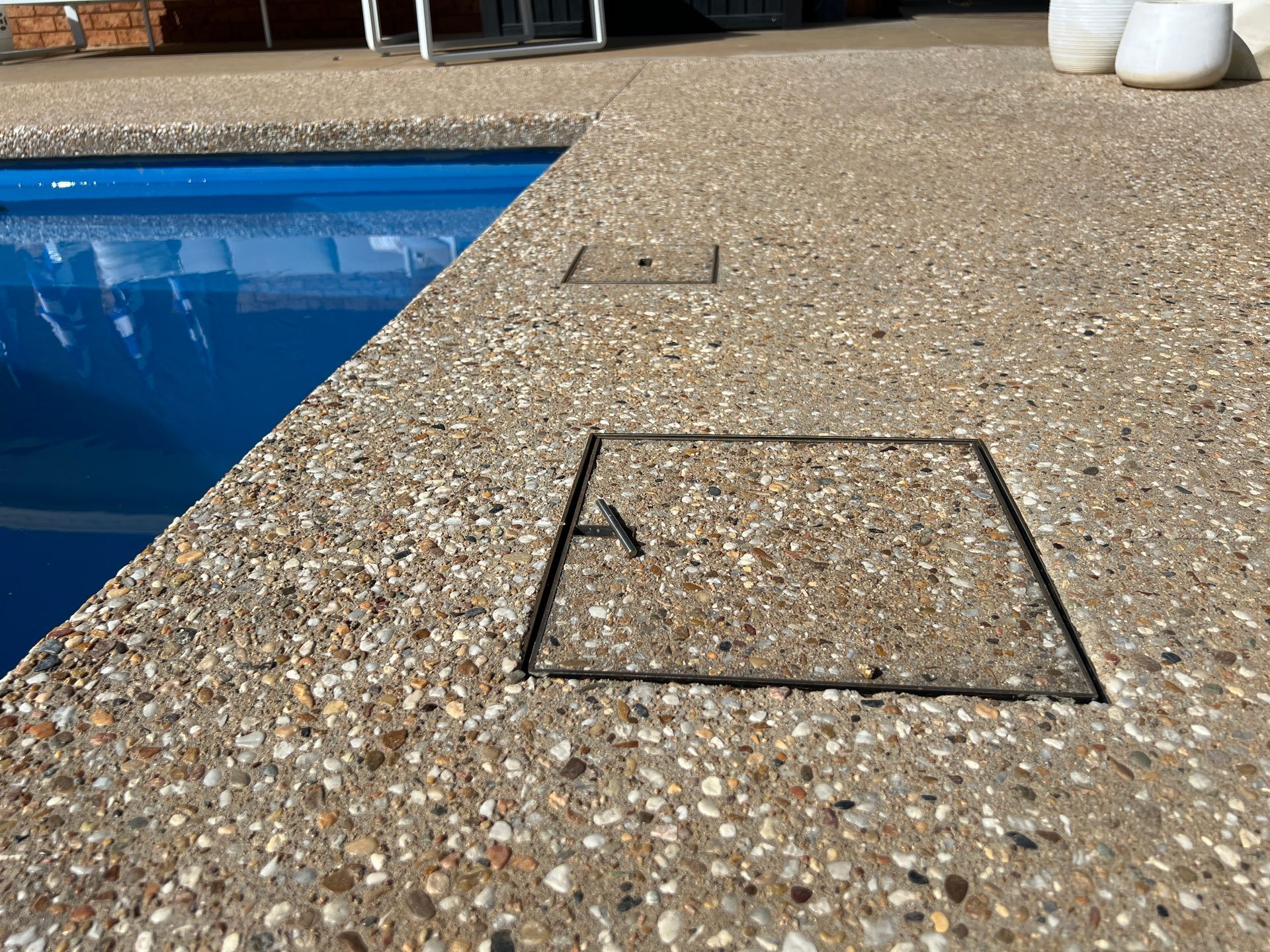 Concrete pool deck with blue water. Two square covers are flush with the surface.