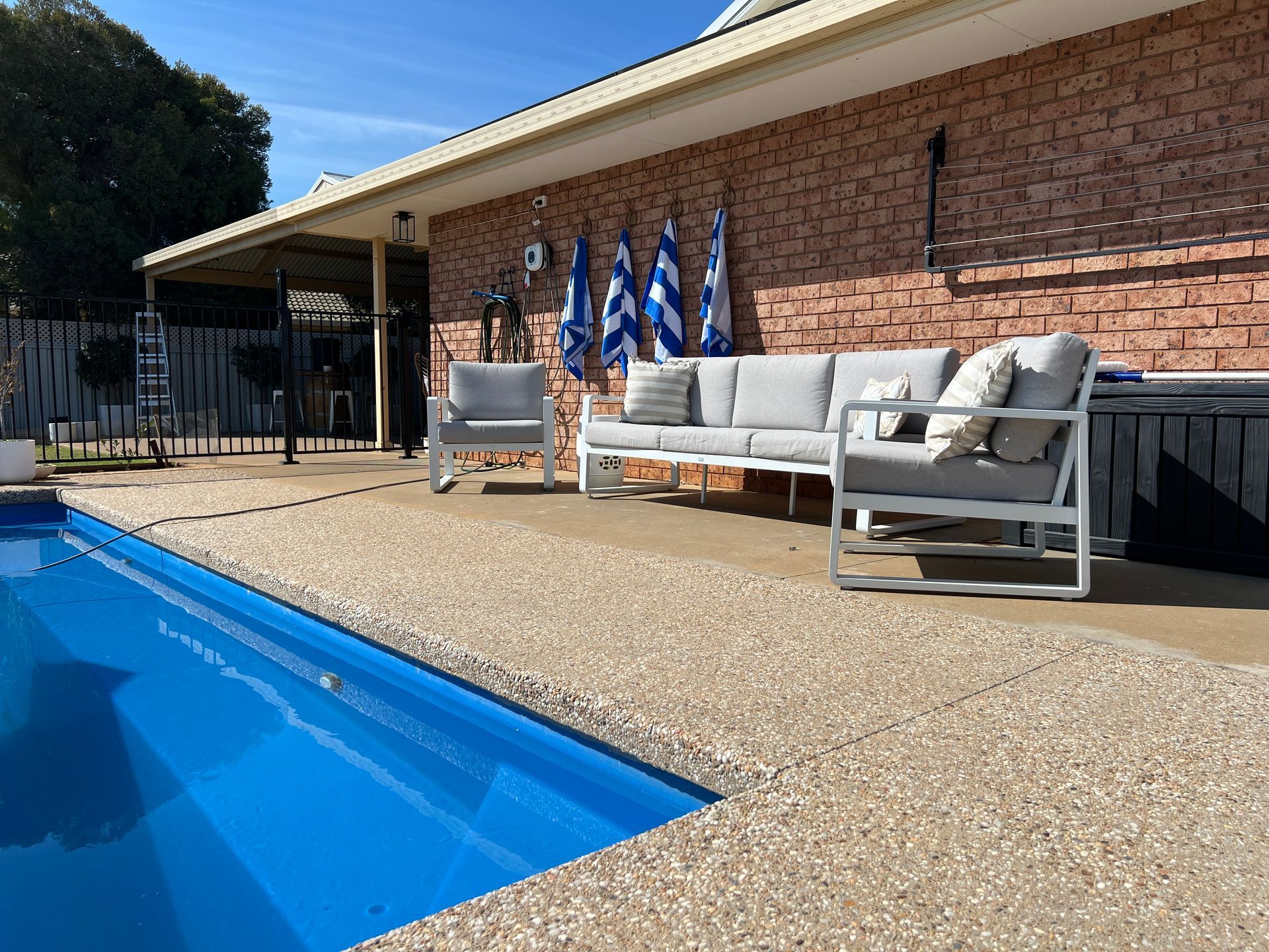 Poolside seating area with gray furniture, blue pool, brick wall, and striped towels.